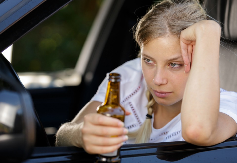 Driver holding a beer bottle while sitting in a vehicle after an alcohol-related incident