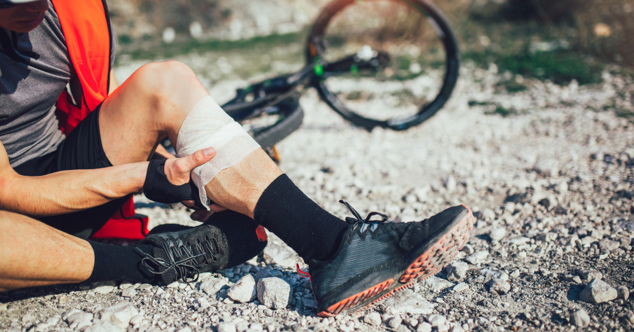 Injured cyclist with a bandaged knee beside a bicycle