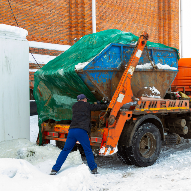 Orange garbage truck collecting trash in a snowy neighborhood