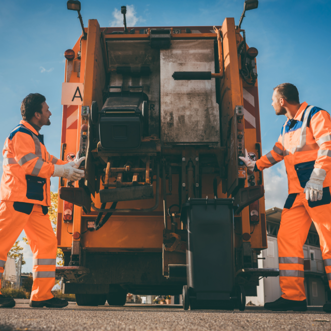 Sanitation workers at the rear of a garbage truck