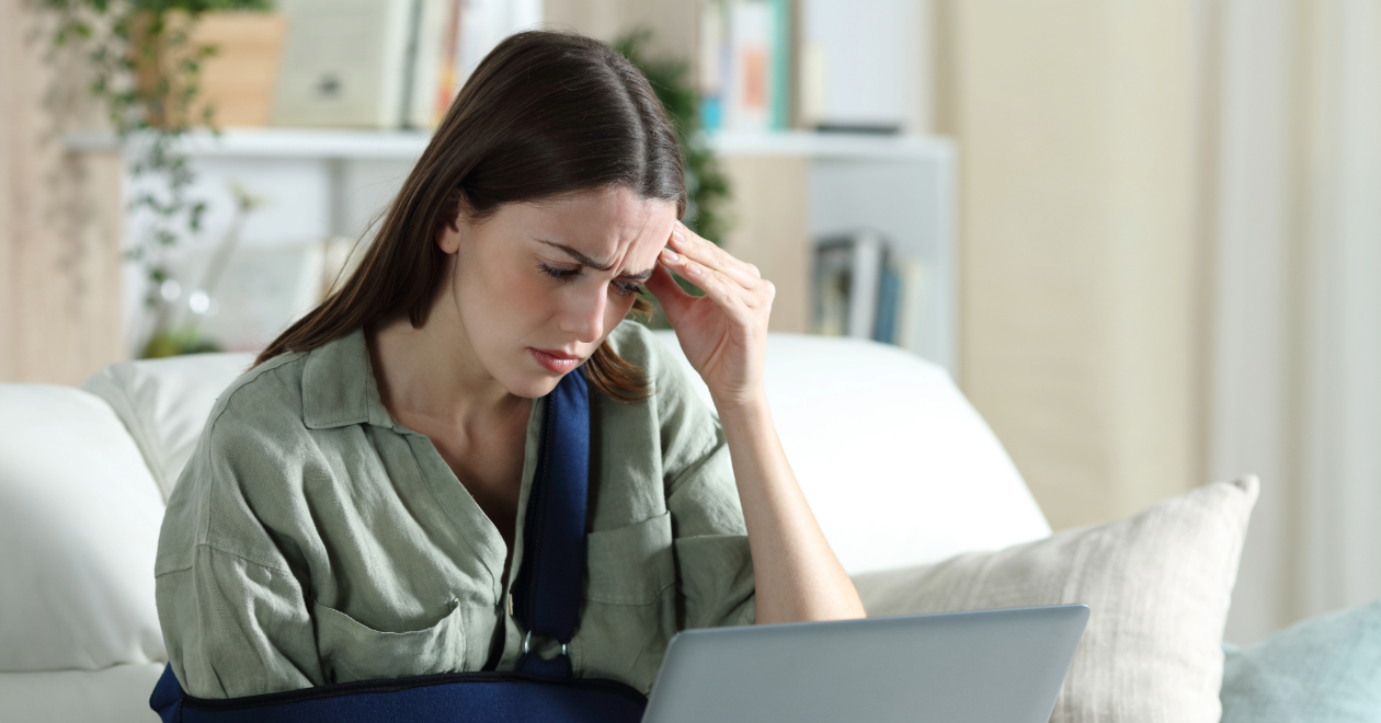 Injured woman with arm sling reviewing insurance paperwork on a laptop
